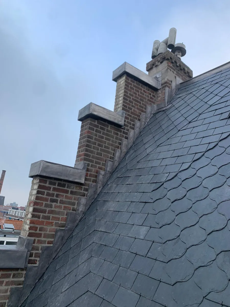 Leien dak met metalen aansluiting langs een gemetselde trapgevel